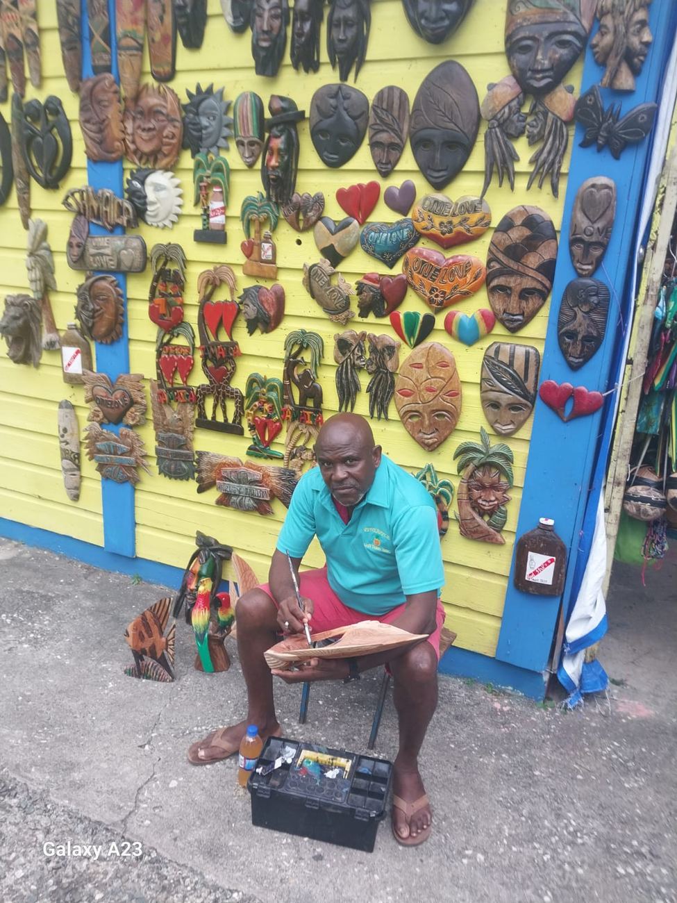 Carved wooden masks, hearts and 'One Love' plaques covering a yellow shopfront wall