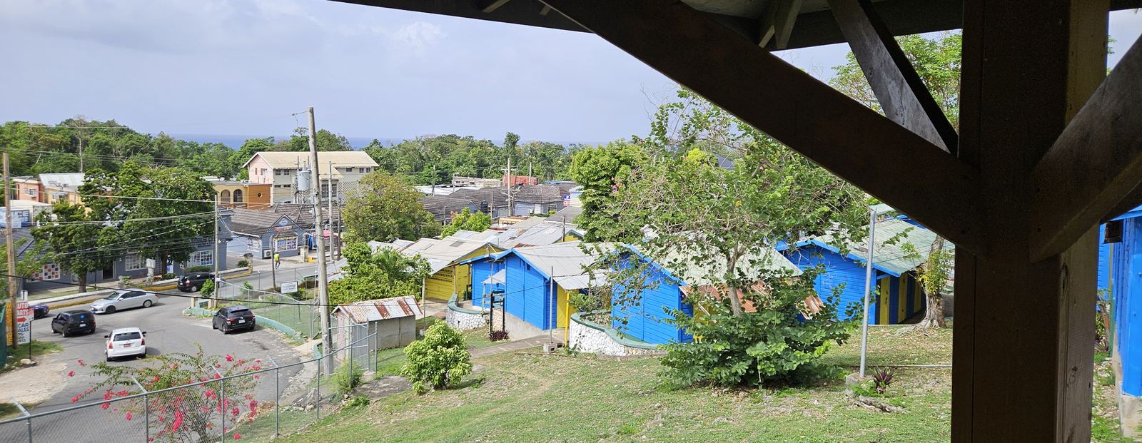 View from under the market's roofline across the blue and yellow shopfronts of Pineapple Craft Market, with the Caribbean Sea on the horizon