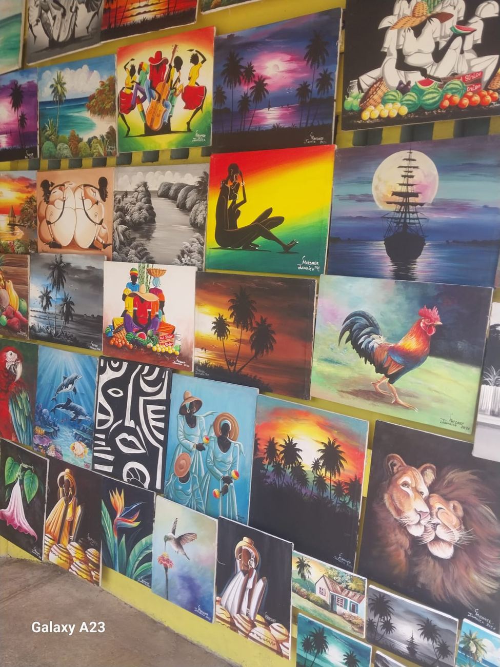 A shopfront wall covered edge to edge with dozens of signed original canvas paintings of Jamaican beaches, dancers, animals and portraits
