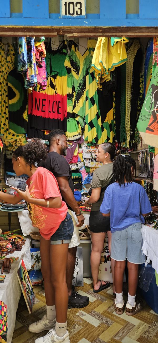 Shoppers browsing Jamaican flags, resort wear and canvas art at shop 103, painted blue with the stall number on the door frame